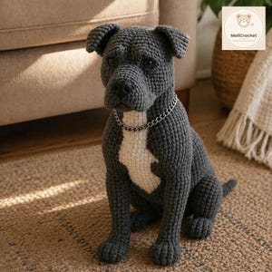 May include: A dark gray crocheted dog figurine with a white chest patch and a silver-toned metal chain collar. The stuffed animal features dark eyes, a textured yarn surface, and is depicted in a seated position with its front paws forward.