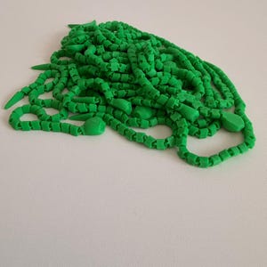 May include: A pile of bright green, articulated plastic chain links. The chain consists of small, repeating square-shaped segments connected together, interspersed with occasional pointed, spike-like components and rounded, bulbous end pieces.