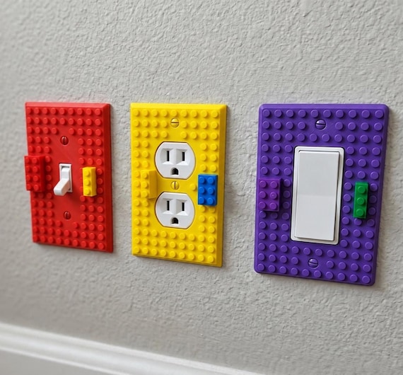 BuildBoard red toggle, yellow 2-Gang outlet, and purple rocker wall plates installed on a textured wall