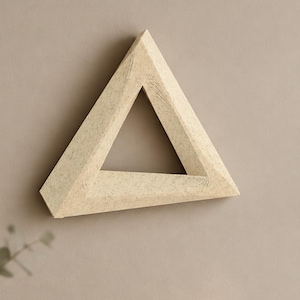 May include: A triangular frame with a speckled off-white finish and a visible wood grain texture. The object features three thick, angled sides that meet at sharp points, creating a hollow center in the shape of an equilateral triangle.