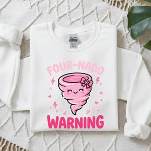 May include: A white long-sleeve sweatshirt featuring a graphic of a smiling pink tornado with a small flower bow. The text above reads FOUR-NADO and the text below reads WARNING in pink lettering, surrounded by small pink lightning bolts and hearts.