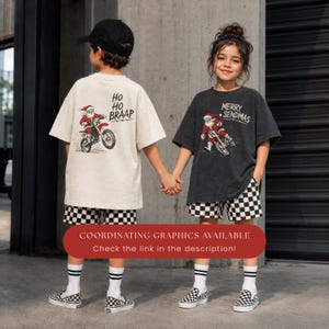 May include: A beige t-shirt with a graphic of Santa Claus on a dirt bike and the text HO HO BRAAP, and a charcoal gray t-shirt with a graphic of Santa Claus on a dirt bike and the text MERRY SENDMAS, both paired with black and white checkered shorts.