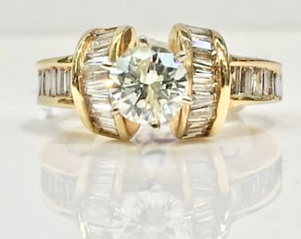 May include: A gold ring with a large round diamond in the center and smaller baguette diamonds set in the band.