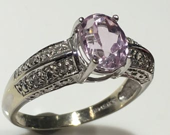 May include: A silver ring featuring a light pink oval gemstone surrounded by smaller clear gemstones.
