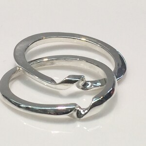 May include: Two silver interlocking rings, one with a twisted design, are shown on a white background.