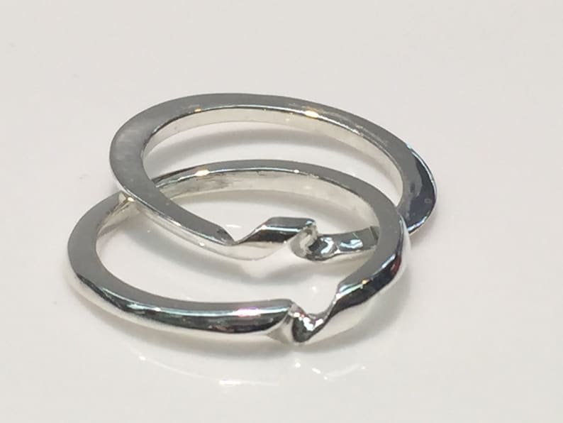 May include: Two silver interlocking rings, one with a twisted design, are shown on a white background.