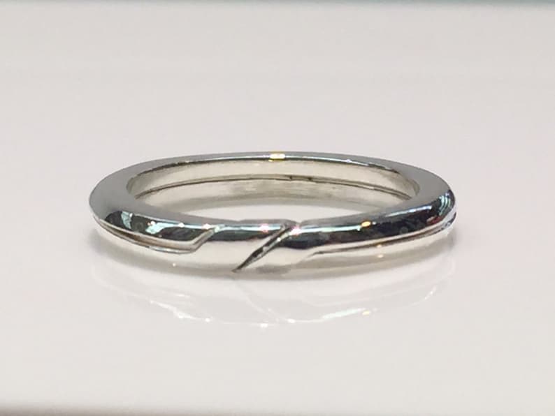 May include: A silver band ring with a unique twisted design. The ring is smooth and polished.