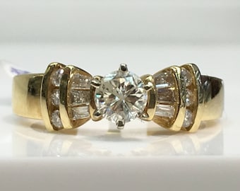 May include: A gold ring with a large round diamond in the center and smaller diamonds on the band. The band is shaped like a bow.
