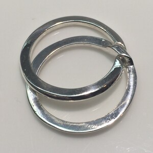 May include: Two interlocking silver rings, one slightly larger than the other, with a smooth, polished finish.