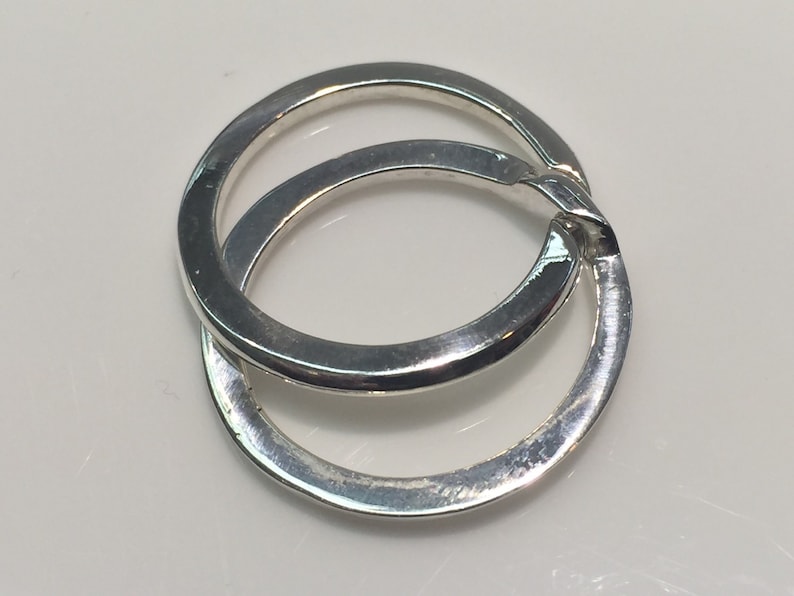 May include: Two interlocking silver rings, one slightly larger than the other, with a smooth, polished finish.
