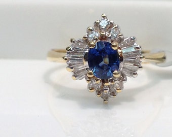 May include: A gold ring with a blue oval sapphire surrounded by a cluster of small diamonds.