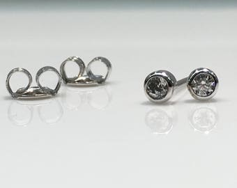 May include: A pair of silver stud earrings with clear round gemstones. The earrings have a butterfly back.