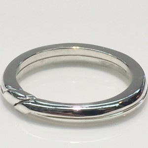 May include: A silver ring with a unique interlocking design. The ring is smooth and polished.