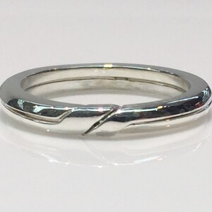 May include: A silver band ring with a unique, twisted design. The ring is smooth and polished.