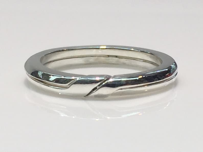 May include: A silver band ring with a unique, twisted design. The ring is smooth and polished.