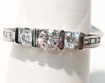 Könnte beinhalten: Ein silberner Ring mit vier runden, klaren Edelsteinen und vertikalen Akzenten aus dunklem Metall. Das Band weist kleine rechteckige Details auf. Der Ring wird vor einem weißen Hintergrund präsentiert.