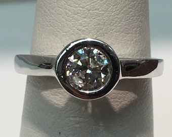 Könnte beinhalten: Ein silberner Ring mit einer Zargenfassung mit einem runden, klaren Diamanten.
