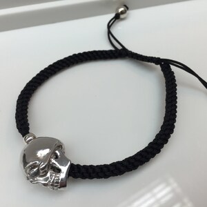 May include: A black braided bracelet with a silver skull charm and silver bead accents.