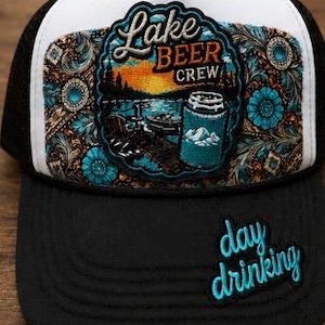 May include: A black and white trucker hat featuring a central patch with a sunset lake scene, a beer can, and the text Lake Beer Crew. The front panel displays a brown and turquoise floral pattern, while the black brim features the text day drinking.