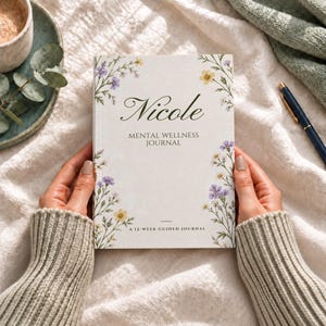 Peut inclure: Un journal blanc avec le texte Nicole MENTAL WELLNESS JOURNAL A 12-WEEK GUIDED JOURNAL imprimé sur la couverture. La couverture présente une illustration botanique délicate de petites fleurs sauvages jaunes et violettes sur les bords.