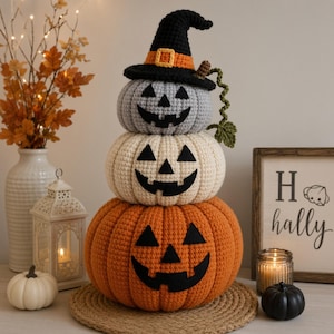 May include: A stacked crochet pumpkin trio featuring a top grey pumpkin wearing a black witch hat with an orange band, a middle cream pumpkin, and a bottom orange pumpkin. Each pumpkin has a black felt jack-o'-lantern face with triangular eyes.