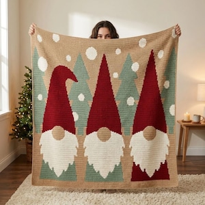 May include: A rectangular crochet blanket featuring a winter scene with three gnomes wearing tall red hats. The background is tan with light green pine trees and white circular snowflakes. The gnomes have large white beards and tan noses.