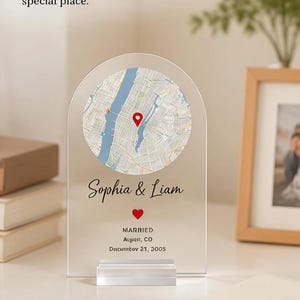 May include: An arched clear acrylic plaque featuring a circular map with a red location pin. The text reads: Thoughtful Keepsake, A daily reminder of your special place, Sophia & Liam, MARRIED, Aspen, CO, December 21, 2005, with two red hearts.