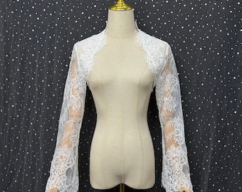 May include: A white lace bolero jacket featuring long sleeves with a floral pattern and scalloped edges. The garment is displayed on a beige mannequin torso. The word Tomorrow is printed in white script in the upper left corner of the image.