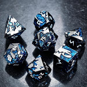 May include: A set of seven polyhedral dice featuring a metallic black finish with deep blue marbled resin inlays. Each die has sharp edges and silver-colored engraved numbers in a stylized font, including a d20, d12, d10, d8, d6, d4, and percentile die.
