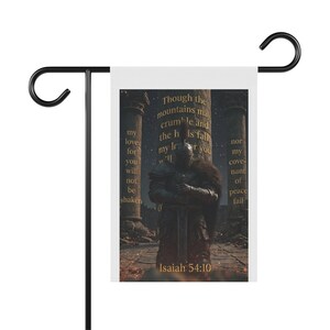May include: A rectangular garden flag hanging on a black metal stand. The flag features a dark, armoured warrior standing between stone pillars with the text: Though the mountains may crumble and the hills fall, my love for you will not be shaken nor my covenant of peace fail. Isaiah 54:10.