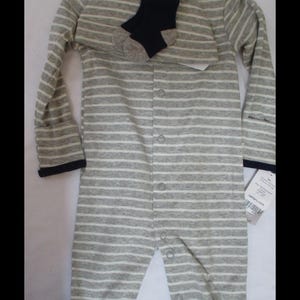 May include: A long-sleeved, footed sleeper with a gray and white horizontal striped pattern, featuring a dark navy blue collar and sleeve cuffs. The garment includes a front snap closure, a matching beanie, and a pair of dark navy blue socks.