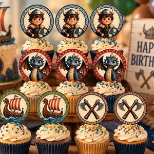Op de afbeelding: Een verzameling cupcake-toppers met ronde ontwerpen van een cartoon-viking, een zwarte draak, een vikingschip en gekruiste bijlen. De toppers staan op cupcakes, met een verjaardagstaart en een bord op de achtergrond.