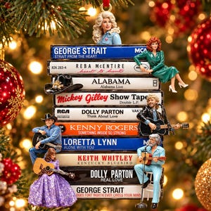 May include: A decorative Christmas tree ornament featuring a stack of nine cassette tapes labelled with country music artists including George Strait, Reba McEntire, Alabama, Mickey Gilley, Dolly Parton, Kenny Rogers, Loretta Lynn, and Keith Whitley.
