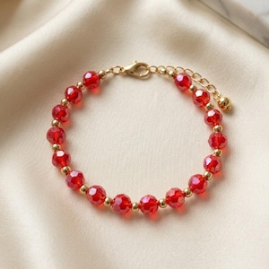 Puede incluir: Una pulsera que alterna cuentas de cristal rojo facetado con pequeñas esferas de metal dorado. La pieza incluye un cierre de mosquetón dorado y una cadena de extensión ajustable terminada con una pequeña cuenta de metal dorado.