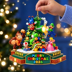 May include: A decorative Christmas tree ornament featuring Mario, Luigi, Donkey Kong, Yoshi, Bowser, Princess Peach, and Toad. The base displays the text MERRY CHRISTMAS 2026, and the green tree includes a pipe with the name ALBERT printed on it.