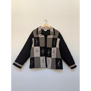May include: A quilted jacket featuring a patchwork design of black, beige, and houndstooth squares. The front panels are decorated with embroidered diamond shapes containing botanical sprigs. It has a collar, long sleeves, and buttons.