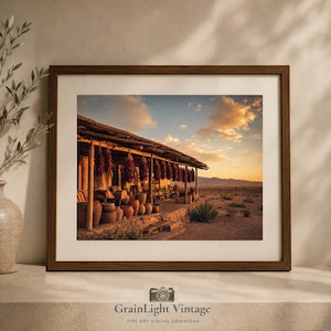 May include: A framed wall art print featuring a desert landscape at sunset. The image shows a rustic porch with rows of hanging red chili peppers, various clay pottery vessels, and wooden chairs, set against a vast, arid horizon under a golden sky.