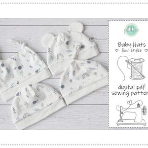 May include: Four baby hats in various styles, each with a white background and a playful pattern of rainbows, snails, and leaves in gentle blue and grey hues. The hats are arranged on a light wood-effect surface. A digital PDF sewing pattern is also shown.
