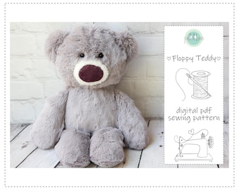 May include: A plush, gray teddy bear with a dark burgundy nose and mouth. The bear is sitting on a light-colored wooden surface. A digital PDF sewing pattern is displayed on a white card, with the text "Floppy Teddy".