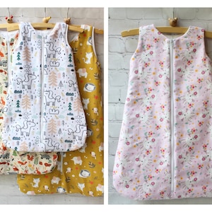 May include: Baby sleep sacks in various patterns, including woodland animals, unicorns, and floral designs. Each sack features a full-length zipper and is sleeveless. The sacks are displayed on wooden hangers.