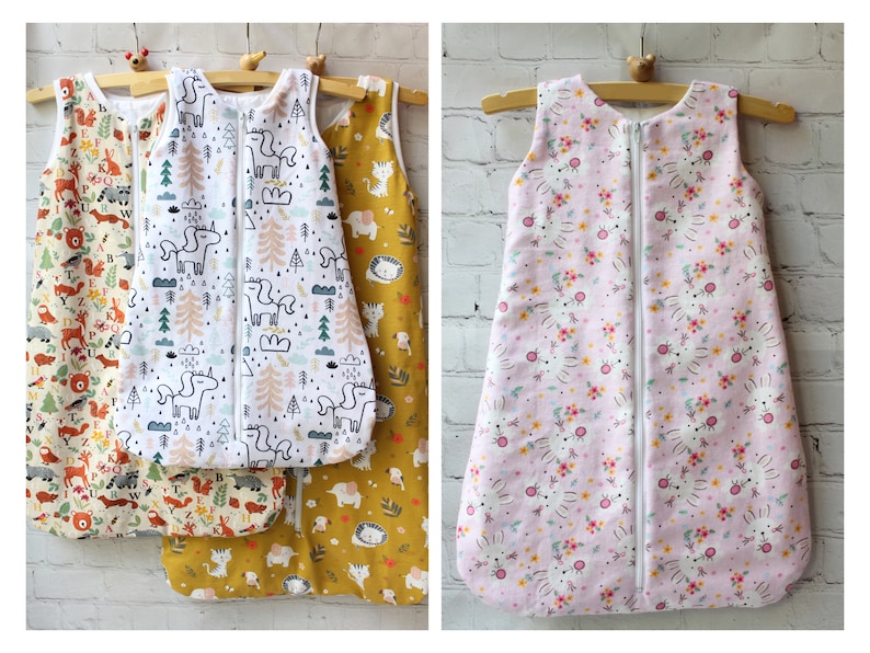 May include: Baby sleep sacks in various patterns, including woodland animals, unicorns, and floral designs. Each sack features a full-length zipper and is sleeveless. The sacks are displayed on wooden hangers.