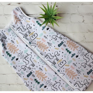 May include: White baby sleep sack with a whimsical unicorn and forest pattern. The design includes outlines of unicorns, trees, clouds, and geometric shapes in black, peach, green, and blue. A white zipper runs down the center.