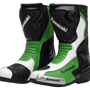 Puede incluir: Un par de botas de moto Kawasaki en negro, blanco y verde. Las botas presentan un diseño de caña alta con paneles protectores, un deslizador de puntera reforzado con el logo de Kawasaki y marcas adicionales en la espinilla y los laterales.