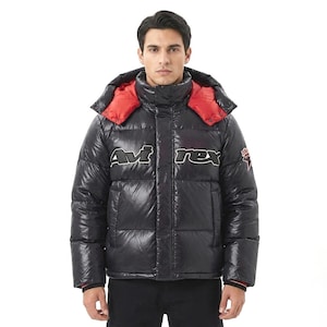 May include: A black puffer jacket with a glossy finish, featuring a hood with a bright red interior lining. The word "Avi" is printed on the left chest and "rex" on the right chest in white letters with black outlines. A small graphic patch is on the left sleeve.