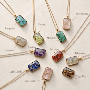 Peut inclure: Une collection de colliers dorés avec des pendentifs rectangulaires remplis de pierres concassées et de flocons d'or. Les pierres étiquetées incluent Turquoise, Péridot, Quartz rose, Amazonite, Malachite, Améthyste, Jaspe rouge, Labradorite, Lapis-lazuli et Œil de tigre.