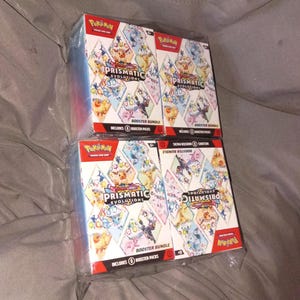 May include: Four sealed Pokémon Scarlet & Violet Prismatic Evolutions booster bundle boxes arranged in a two-by-two grid. Each white box features colorful diamond-shaped illustrations of various Eevee evolutions and the Prismatic Evolutions logo.