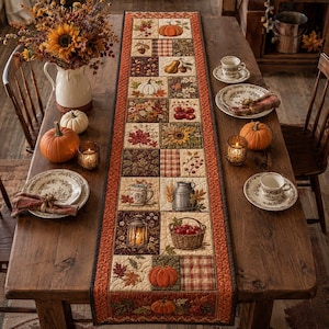 Könnte beinhalten: Ein rechteckiger, gesteppter Tischläufer mit einem Patchwork-Design aus herbstlichen Quadraten, darunter Kürbisse, Sonnenblumen, Blätter, Beeren, eine Laterne und ein Korb mit Äpfeln, eingefasst von einem rostorangen Stoff mit dunkelbraunem Rand.