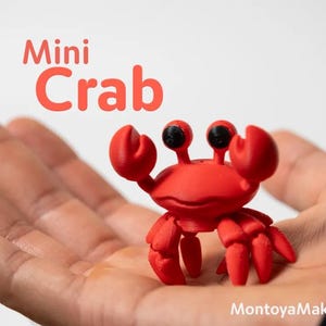 May include: A small, bright red crab figurine with two raised claws and prominent black eyes. The text 'Mini Crab' appears in red above the figure, and 'MontoyaMaker' is printed in white in the bottom right corner of the image.