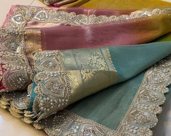 May include: A multi-colored saree featuring a gradient of teal, pink, and yellow fabric. The border is heavily embellished with intricate silver embroidery, metallic gold accents, small white pearls, and reflective mirror-like circular inserts.