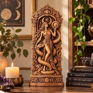 Könnte beinhalten: Eine hohe, braune, harzähnliche Skulptur mit einer zentralen weiblichen Figur inmitten gewundener Schlangen. Die Figur hält eine Kugel, eingerahmt von einem verzierten Torbogen mit himmlischen Mondmotiven. Der Sockel zeigt komplexe Schnitzereien der Mondphasen.